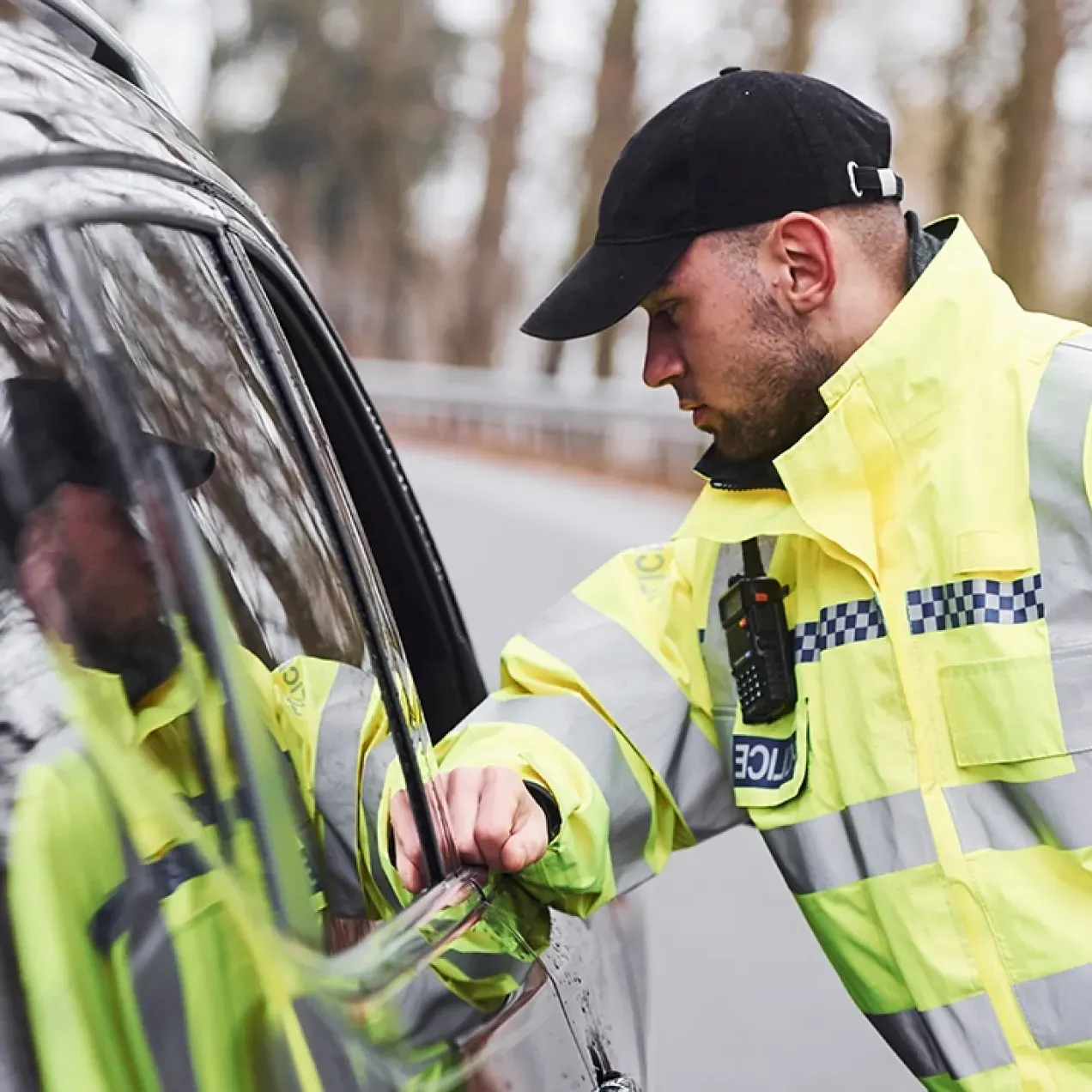 A Herzing University criminal justice graduate in a high-visibility police jacket conducts a routine traffic stop on a rural road.